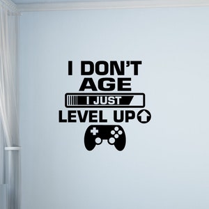 Könnte beinhalten: Schwarz-weiße Wanddekoration mit dem Text "Ich werde nicht älter, ich level einfach nur auf" und einer Grafik eines Videospiel-Controllers.