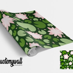 May include: A roll of green and pink patterned wallpaper with a repeating design of lily pads and water lilies. The wallpaper is rolled up and the end of the roll is visible. The text "quotemywall vinyl & prints" is visible at the bottom of the image.