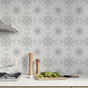 May include: A kitchen backsplash with a gray and white geometric pattern. The backsplash is made of ceramic tiles and features a repeating design of white circles with intricate details on a gray background. The backsplash is installed behind a stovetop and a stainless steel range hood.
