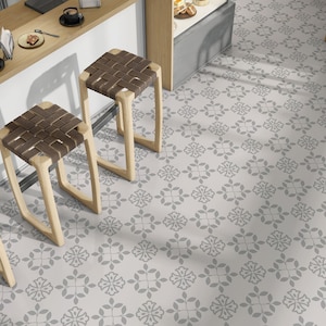 May include: Three wooden bar stools with brown woven seats, arranged in a row against a white wall with a patterned grey tiled floor.