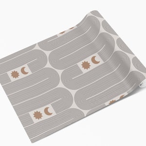 Puede incluir: Un rollo de papel pintado con un patr&oacute;n repetitivo de l&iacute;neas curvas grises y fondo beige. El dise&ntilde;o incluye formas de sol y luna creciente marrones. El papel pintado est&aacute; enrollado, mostrando el patr&oacute;n en la superficie.
