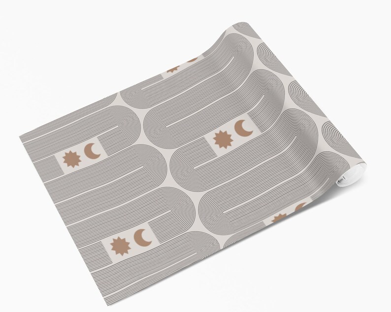 Puede incluir: Un rollo de papel pintado con un patr&oacute;n repetitivo de l&iacute;neas curvas grises y fondo beige. El dise&ntilde;o incluye formas de sol y luna creciente marrones. El papel pintado est&aacute; enrollado, mostrando el patr&oacute;n en la superficie.