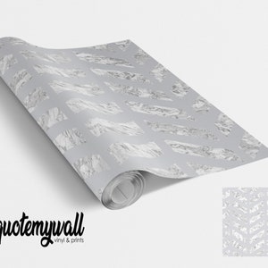 Pode incluir: Um rolo de papel de parede com padrão chevron prata e branco sobre um fundo branco. O papel de parede está enrolado e tem uma etiqueta que diz "quotemywall vinyl & prints".