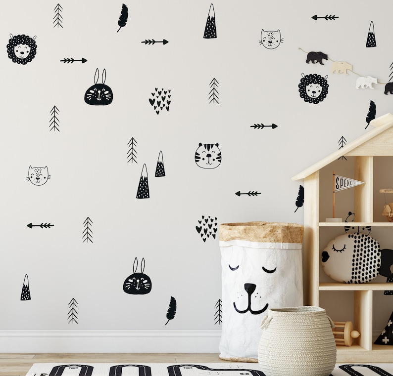 May include: Black and white wall decals featuring various animal and nature designs, including a lion, rabbit, cat, tiger, mountains, trees, arrows, and hearts. The decals are displayed on a white wall with a dollhouse and a storage bin in the foreground.