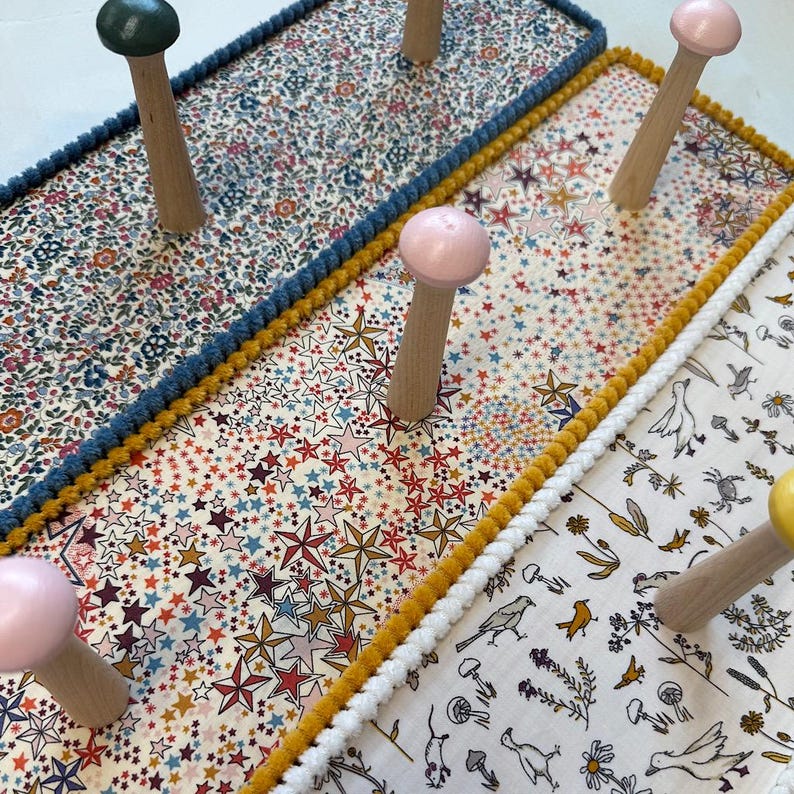 Puede incluir: Tres percheros de pared rectangulares con paneles cubiertos de tela con patrones distintos: un estampado floral, un motivo de estrellas y un dise&ntilde;o de naturaleza con p&aacute;jaros y setas. Cada perchero tiene ganchos de madera con puntas de color.