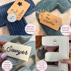 May include: Close-up of corduroy fabric letters in various colors, each with a tag. The tags include names like "Theo" and "Clemmie." One letter has a metal D-hook for hanging. The letters are suitable for nursery decor.