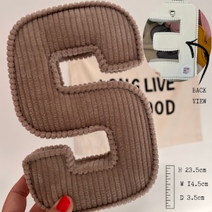 May include: A brown corduroy letter S with a white backing. The letter is 23.5 inches tall, 14.5 inches wide, and 3.5 inches deep. The back of the letter has a loop for hanging.
