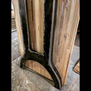 May include: Close-up of a black metal table leg with a curved base. The leg is attached to a wooden tabletop.