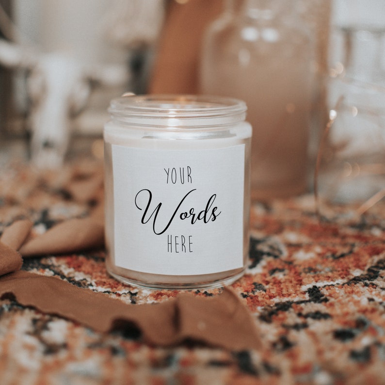 Pu&ograve; includere: Una candela bianca in un barattolo di vetro con un'etichetta bianca che dice "YOUR Words HERE". La candela &egrave; appoggiata su un tappeto a motivi marroni e arancioni.