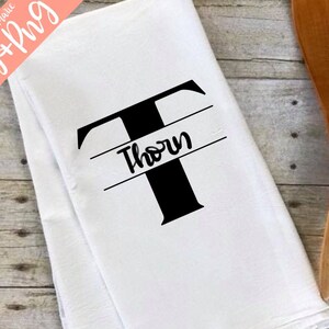 May include: White kitchen towel with a black letter T and the name "Thorn" printed on a horizontal black line above the letter.