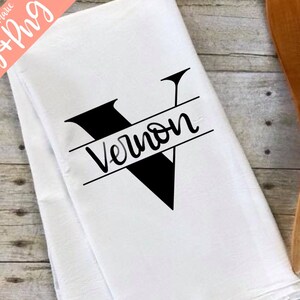 May include: White kitchen towel with a black letter V and the name Vernon written in cursive across the centre.