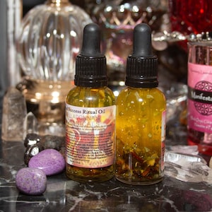 May include: Two small amber glass bottles with gold glitter and herbs inside. The bottles are labeled "Success Ritual Oil" and "Belladonna's Botanicals".