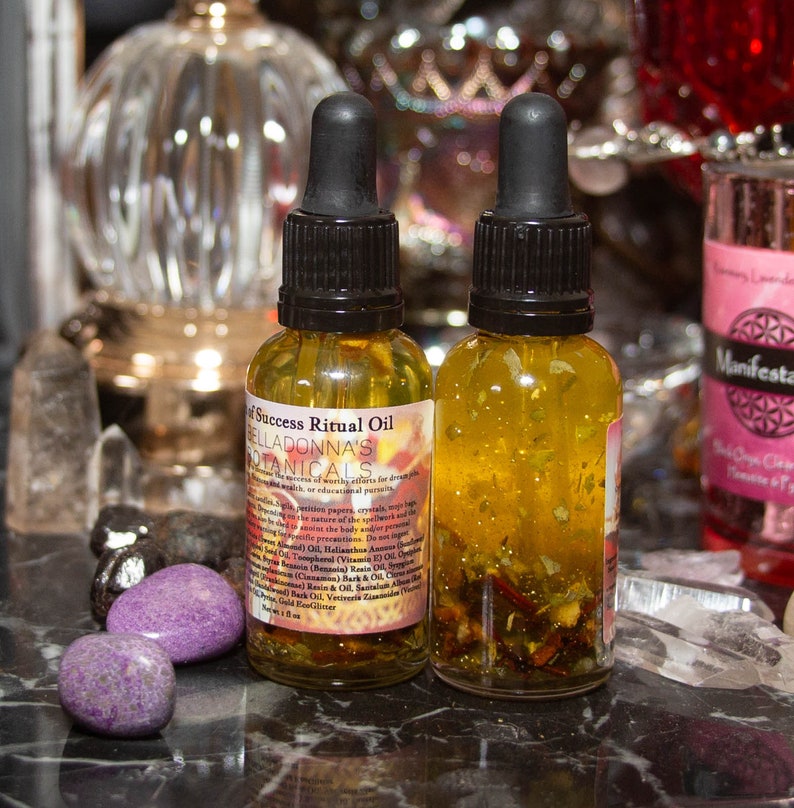 Pu&ograve; includere: Due piccole bottiglie di vetro ambrato con glitter dorati ed erbe al loro interno. Le bottiglie sono etichettate 'Success Ritual Oil' e 'Belladonna's Botanicals'.