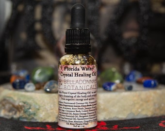 Pode incluir: Um pequeno frasco de vidro com conta-gotas, cheio de um líquido transparente e ervas. O rótulo diz "Florida Water Crystal Healing Oil" e "Belladonnas Botanicals".