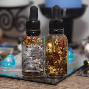 Könnte beinhalten: Zwei kleine Glasflaschen gefüllt mit einer klaren Flüssigkeit und getrockneten Kräutern und Blumen. Die Flaschen haben schwarze Tropfer und sind mit "Mind Control Spell Oil" und "Belladonna Botanica" beschriftet.