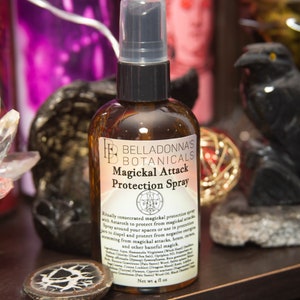 May include: A brown glass bottle with a clear spray nozzle. The bottle is labeled "BellaDonna's Botanicals Magickal Attack Protection Spray". The label also includes a pentagram symbol and a list of ingredients.