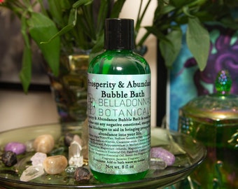 Może przedstawiać: Zielona butelka z pianką do kąpieli Prosperity & Abundance marki Belladonna Botanical. Etykieta głosi: "Prosperity & Abundance Bubble Bath służy do oczyszczania negatywnych emocji i energii, blokując je, aby pomóc w przyniesieniu dobrobytu i obfitości do twojego życia."