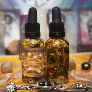 May include: Two amber glass bottles with black dropper tops filled with a clear liquid and dried flowers. The bottles are labeled "Think of Me Ritual Oil" and "Belladonna Botanicals".