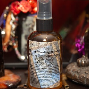 Może przedstawiać: Brązowa butelka ze szkła z czarną dyszą rozpylającą i białą etykietą. Etykieta zawiera napis "BELLADONNA'S BOTANICALS Mirror Warding & Portal Closing Protection Spray". Etykieta zawiera również dwa symbole i listę składników.