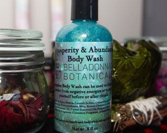 Może przedstawiać: Turkusowa butelka żelu do mycia ciała Prosperity & Abundance marki Belladonna's Botanicals. Butelka jest opisana nazwą produktu i opisem jego zastosowania. Butelka zawiera 8 uncji płynu.