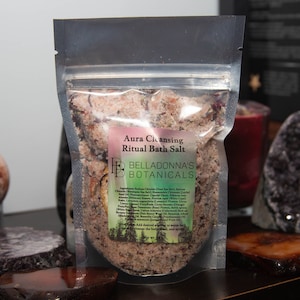 Peut inclure: Un sachet en plastique transparent rempli de sels de bain roses, étiqueté "Aura Cleansing Ritual Bath Salt" et "BELLADONNA'S BOTANICALS". L'étiquette liste les ingrédients, notamment le sel de la mer Morte, le chlorure de sodium, le sel rose de l'Himalaya et des huiles essentielles.