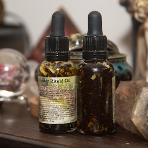May include: Two small amber glass bottles with dropper tops filled with a dark liquid and dried herbs. The bottles are labelled "Muster Ritual Oil" and "BellaDonna's Botanicals".