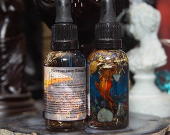 Peut inclure: Deux petites bouteilles en verre remplies d'un liquide clair et de diverses herbes et fleurs séchées. Les bouteilles ont des bouchons compte-gouttes noirs et des étiquettes qui indiquent "Necromancy Ritual Oil" et "Belladonna Botanical".