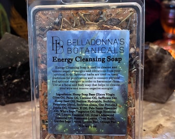 Può includere: Una saponetta rettangolare Energy Cleansing Soap di Belladonna's Botanicals in una confezione di plastica trasparente. Il sapone è marrone e contiene erbe essiccate, tra cui foglie di rosmarino, chiodi di garofano e scorze di agrumi.