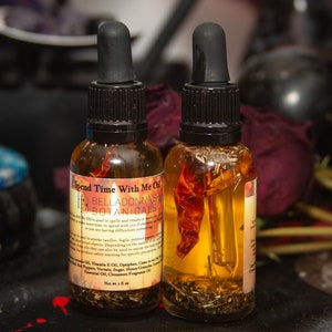May include: Two glass bottles of oil with black droppers. The bottles contain herbs and spices, including a red pepper. The label reads "Spend Time With Me Oil" by Belladonna's Botanicals. Each bottle is 1 fl oz.