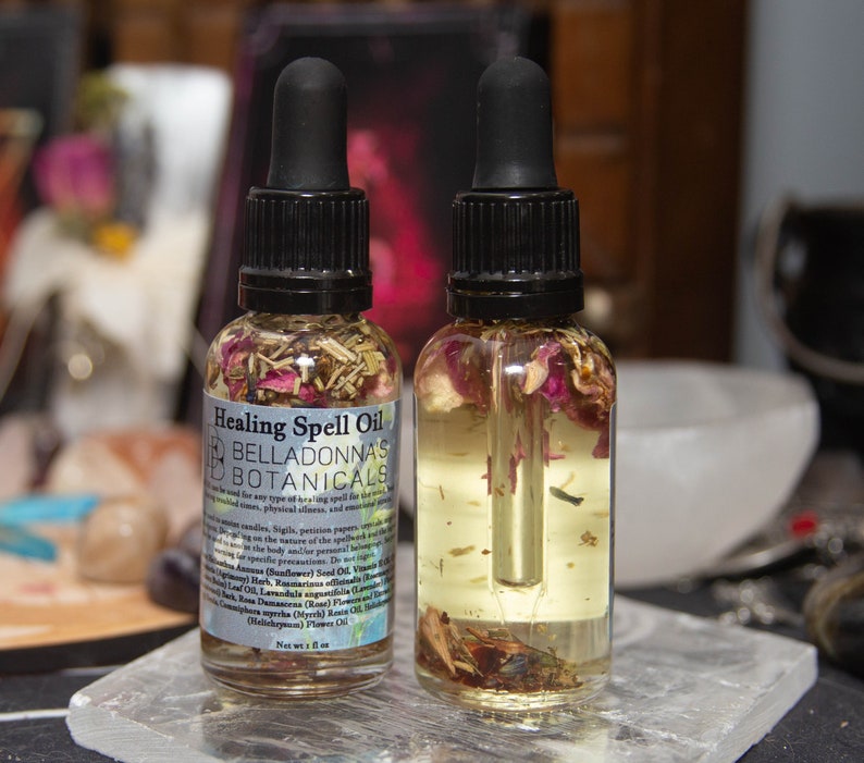 May include: Two small glass bottles filled with a clear liquid and dried herbs and flowers. The bottles have black dropper tops and labels that read "Healing Spell Oil" and "Belladonna's Botanicals".