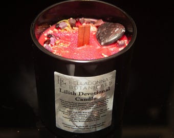 May include: A black glass candle jar with a red candle inside. The candle is topped with a wooden wick and crystals. The label on the jar reads "Belladonna's Botanicals Lilith Devotional Candle". This candle is a blend of Poppy, Patchouli, Rose, Vanilla, Orchid, Jasmine, Cinnamon, Sandalwood, and Myrrh. It is intended for offering or use in any spell and ritual.