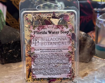 Pode incluir: Uma embalagem retangular de plástico transparente contendo sabonete Florida Water da Belladonna's Botanicals. O sabonete está incrustado com pétalas de flores secas, ervas e especiarias. Um rótulo central exibe o nome, a marca e os ingredientes.