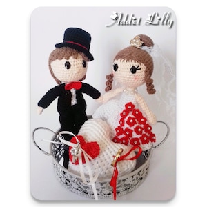 May include: Crocheted bride and groom figurines holding a white heart-shaped pillow with red accents. The figurines are sitting on a silver tray with a decorative design.