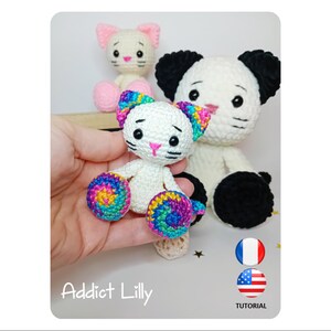 May include: Crocheted cat toys in white, pink, and black. One cat is held in a hand, showcasing rainbow-colored accents on the ears and paws. The image includes the text "Addict Lilly" and flags for the USA and France, with the word "TUTORIAL".