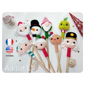Peut inclure: Une collection de dessus de crayons de Noël faits à la main au crochet. Les dessus comprennent le Père Noël, un bonhomme de neige, un gnome, un Grinch, un bonhomme en pain d'épices et un casse-noisette. Les crayons sont sur une surface blanche avec le texte "Addict Lilly" et "TUTORIAL".