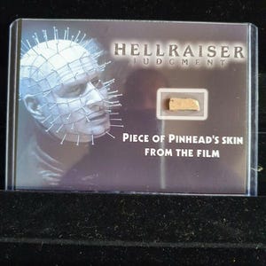 Może przedstawiać: Karta kolekcjonerska z logo Hellraiser Judgment i portretem Pinheada z gwoździami w głowie. Karta zawiera również mały kawałek skóry Pinheada z filmu.