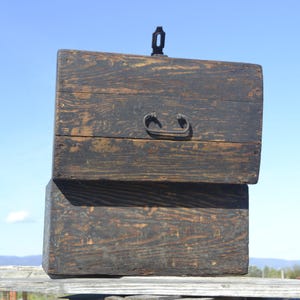 May include: A dark brown wooden chest with two lids and metal handles. The chest is weathered and has a rustic appearance.