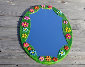 May include: Oval mirror with a green frame decorated with colorful flowers made of mosaic tiles.