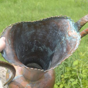 May include: A large copper pitcher with a scalloped rim and a hammered handle. The pitcher has a green patina and is in good condition.