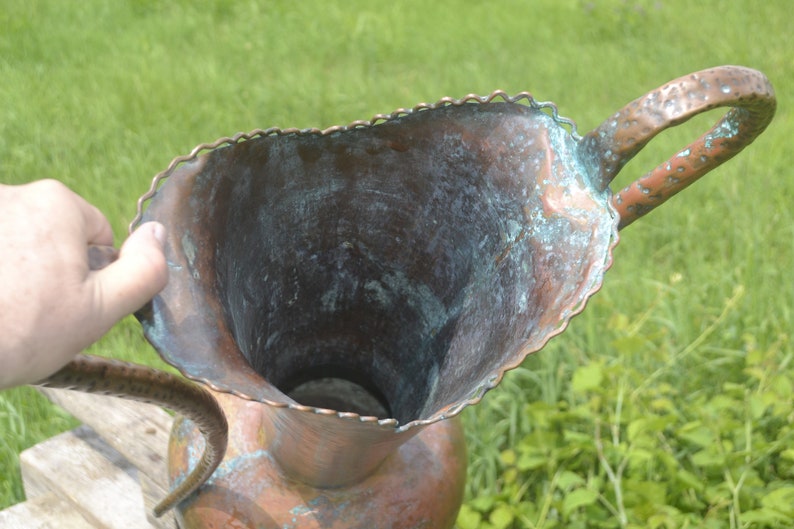 May include: A large copper pitcher with a scalloped rim and a hammered handle. The pitcher has a green patina and is in good condition.