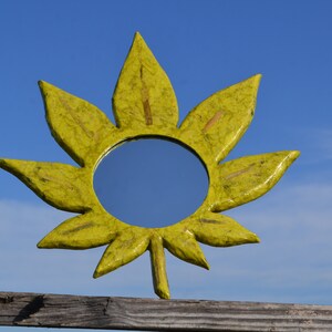 May include: A yellow leaf-shaped mirror with a round reflective surface. The mirror is made of papier-mâché and has a rustic, handmade look.