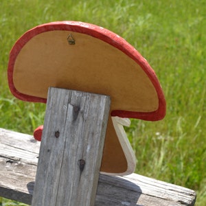 Pu&ograve; includere: Un decoro da parete a forma di fungo rosso e bianco con un retro in cartone marrone. Il decoro ha un gancio di metallo sul retro per appenderlo.