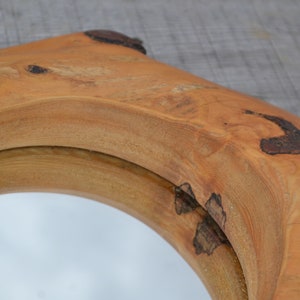 Puede incluir: Un espejo redondo con un marco de madera natural. El marco est&aacute; hecho de una gruesa rebanada de madera con una forma natural y org&aacute;nica. La madera tiene un color marr&oacute;n c&aacute;lido y un acabado liso y pulido.