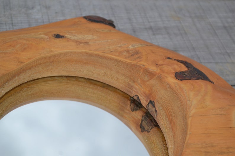 Puede incluir: Un espejo redondo con un marco de madera natural. El marco est&aacute; hecho de una gruesa rebanada de madera con una forma natural y org&aacute;nica. La madera tiene un color marr&oacute;n c&aacute;lido y un acabado liso y pulido.