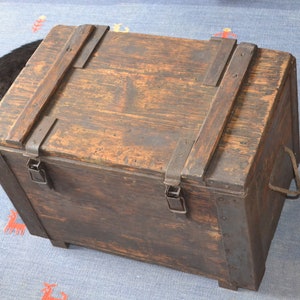 Op de afbeelding: Een vintage houten kist met metalen beslag en een scharnierend deksel. De kist heeft een donkerbruine afwerking en is beveiligd met metalen sluitingen.