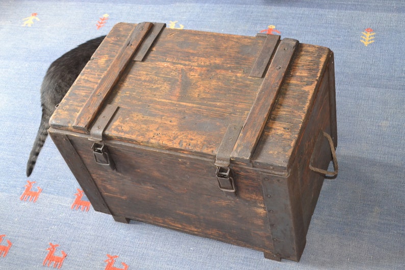 Op de afbeelding: Een vintage houten kist met metalen beslag en een scharnierend deksel. De kist heeft een donkerbruine afwerking en is beveiligd met metalen sluitingen.