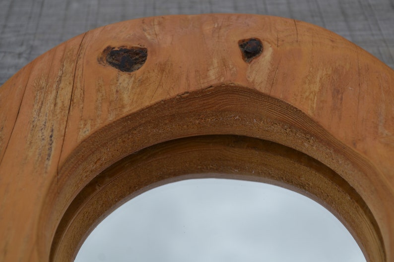 Puede incluir: Un espejo redondo de madera con un acabado de madera natural. El espejo tiene un marco doble con un borde ligeramente elevado. La madera tiene un aspecto r&uacute;stico con nudos y patrones de veta.