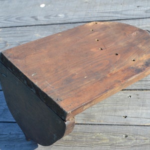 May include: A wooden shelf bracket with a curved top and a dark brown finish. The bracket has several holes drilled into the top surface.