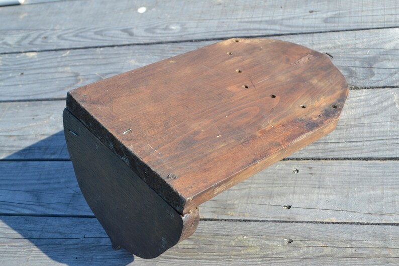 May include: A wooden shelf bracket with a curved top and a dark brown finish. The bracket has several holes drilled into the top surface.