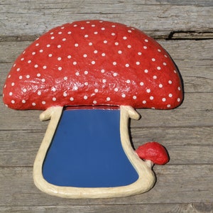 Pu&ograve; includere: Uno specchio a forma di fungo rosso e bianco a pois con una superficie riflettente blu. Lo specchio &egrave; fatto di cartapesta e ha un gambo bianco.